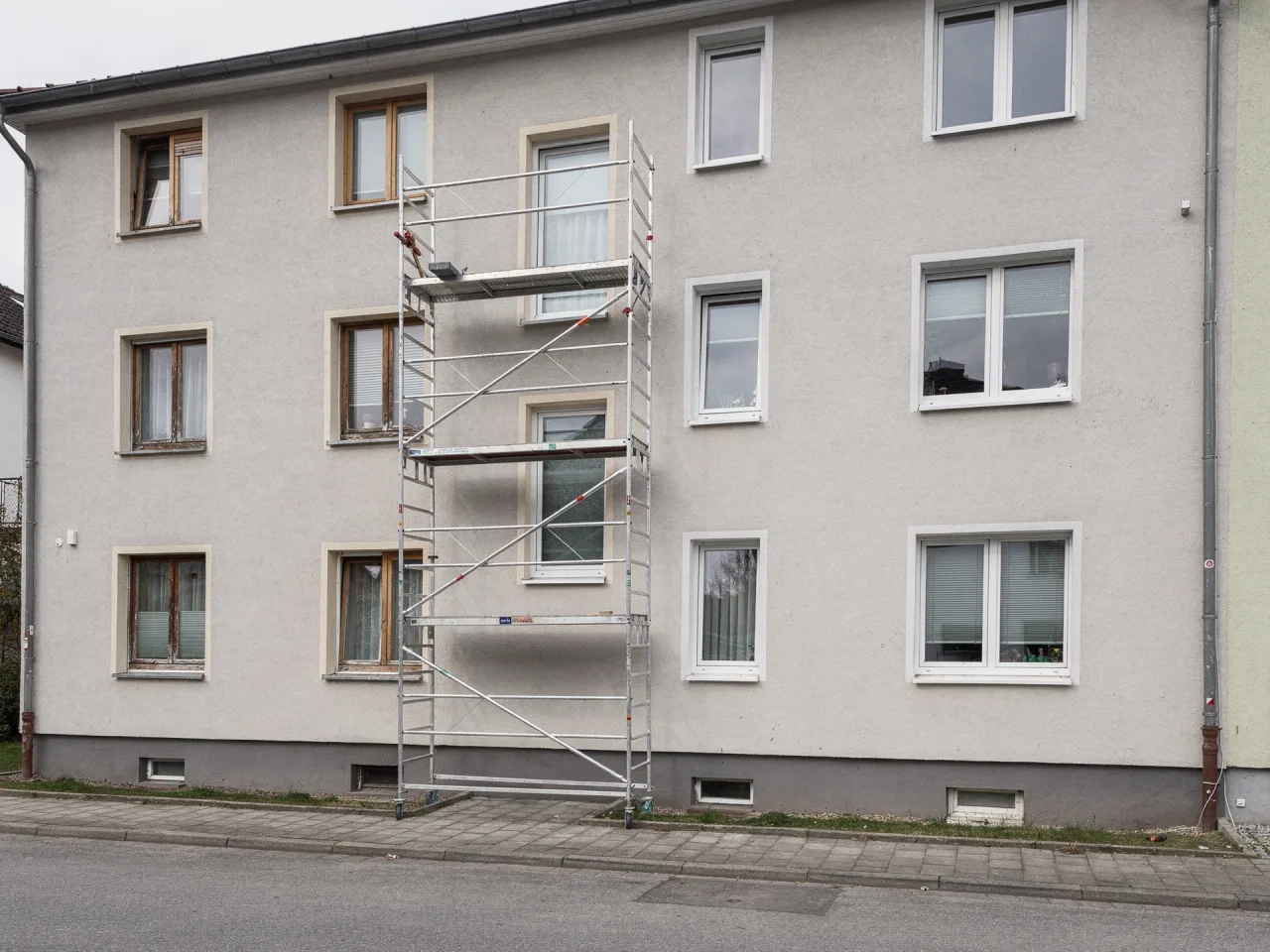Wohngebäude beim Fenstertausch: links noch alte Holzfenster, rechts bereits neue weiße Kunststofffenster