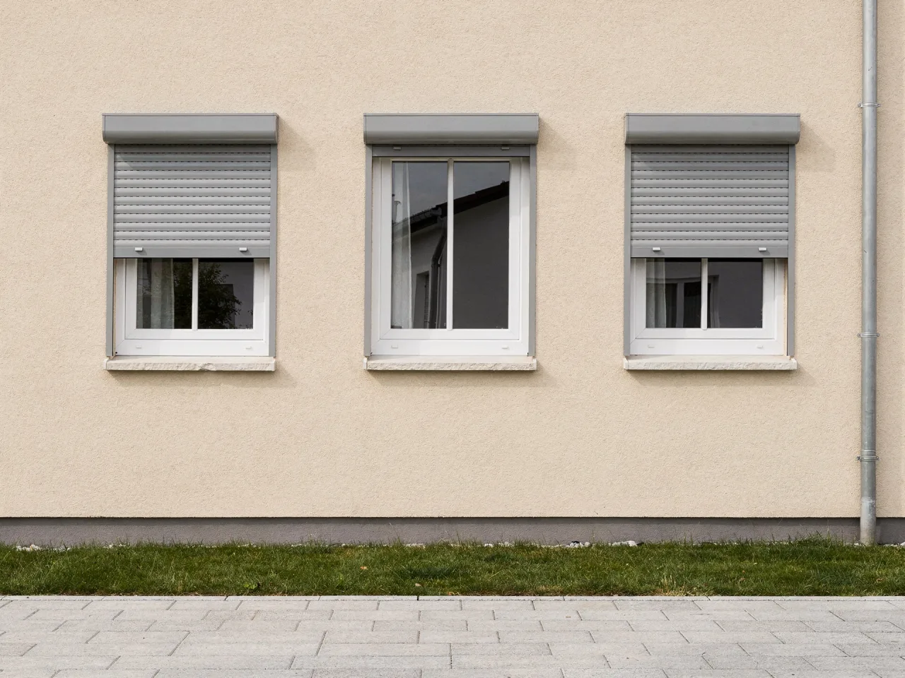 Vorbaurollläden über weißen Fenstern an einer Hausfassade, zwei davon halb herabgelassen